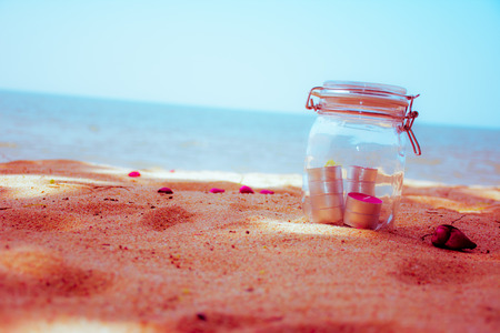 Candles in jar with beautiful beach and sea in background. - vintage filterの写真素材