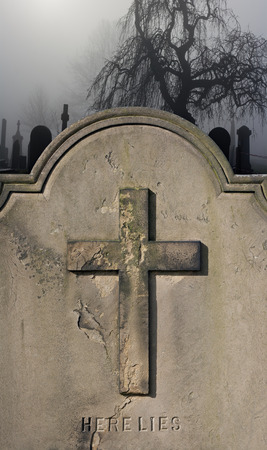 Spooky old weathered headstone in a foggy graveyardの写真素材