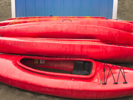 Empty red plastic recreational kayaks for rent or hire, stored on sandy beach after hours on a rainy day.  Crescent Beach, Surrey, British Columbia, Canada.の写真素材