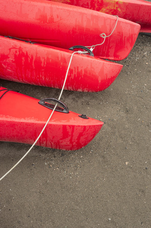 Empty red plastic recreational kayaks for rent or hire, stored on sandy beach after hours on a rainy day.  Crescent Beach, Surrey, British Columbia, Canada.の写真素材