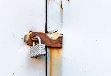 Locked simple metal padlock hanging on rusted hasp on metal doors.の写真素材