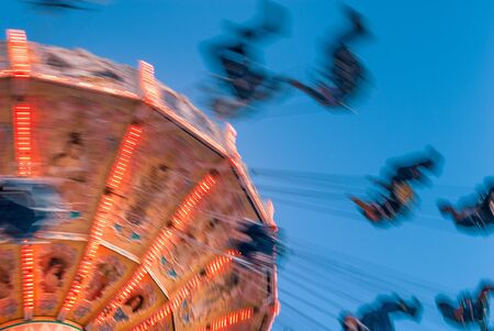 Amusement park motion blurred riders on retro vintage tilting swing against clear blue sky.の写真素材