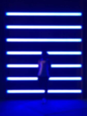 The blurred shadow of an Asian woman standing in front of an expensive face with a blue neon lamp and the light falling onto the ground Photos from the front view.の写真素材