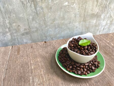 Arabica coffee beans in a cup of beverage and around the cup And with leaves on top are placed on a wooden table, with a background of grunge style coffee break concept. cafe idea.の写真素材