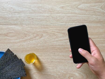 Crispy seaweed with hot green tea, morning snack  And have a Hand man is holding a smartphone on the right background is wood with copy space. Concept for relaxing. Home holiday Simple morning.の写真素材