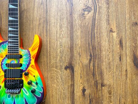 colorful Tie-dye electric guitar made from a genuine mahogany wood Popular musician on veneer brown wood background with copy space on right. business and music concept. Wallpaper or background.の写真素材