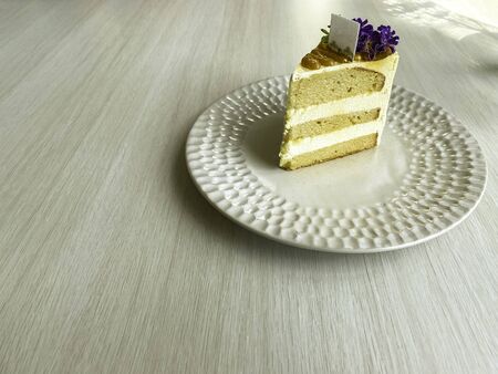 Creamy cake toppings are sweet, fragrant, honey-caramelized, laying out, decorated with purple flowers on a white plate, sprinkled with gold powder, placed on a white wooden table with copy space.の写真素材