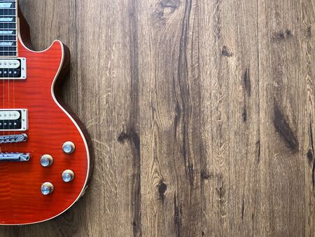 Red electric guitar made from a genuine mahogany wood Popular musician on veneer brown wooden background with copy space on right for letter. business and music concept. Wallpaper or background.の写真素材