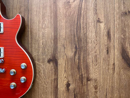 Red electric guitar made from a genuine mahogany wood Popular musician on veneer brown wood background with copy space on right for letter. business and music concept. Wallpaper or background.の写真素材
