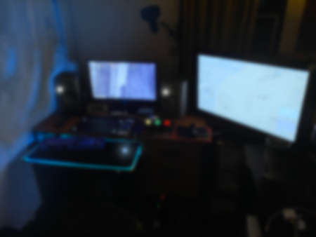 blurred Powerful Personal desktop Computer Gamer Rig with First-Person Shooter Game on Screen.Dual Monitor on wooden Table at Home. Cozy Room with  Blue Neon Light.の写真素材