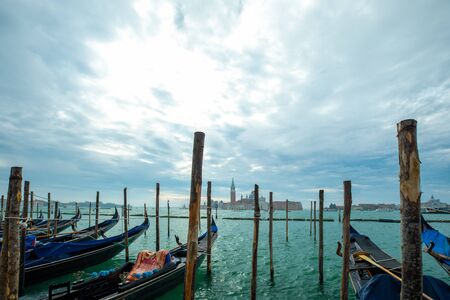 Photograph of Gondola's docked on the shore of Venice, Italy. Cloudy overcast day, surrounded by water.の写真素材