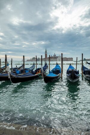 Photograph of Gondola's docked on the shore of Venice, Italy. Cloudy overcast day, surrounded by water.の写真素材