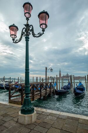 Photograph of Gondola's docked on the shore of Venice, Italy. Cloudy overcast day, surrounded by water.の写真素材