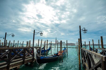 Photograph of Gondola's docked on the shore of Venice, Italy. Cloudy overcast day, surrounded by water.の写真素材