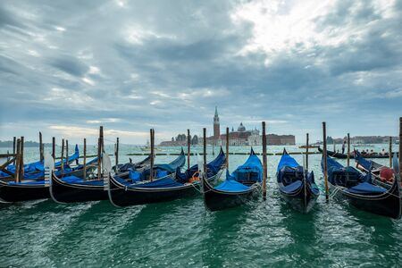 Photograph of Gondola's docked on the shore of Venice, Italy. Cloudy overcast day, surrounded by water.の写真素材