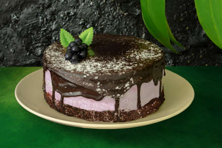 Chocolate berry cake decorated with blueberries on a green table on a black background. And next to...