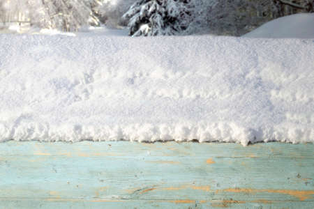 A thick cap of snow on a wooden box against the background of a winter forest with bright sunlight. New year banner with a Christmas mood.の写真素材