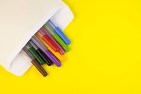 markers of different colors are enclosed in a mail envelope on a yellow background, top view. markers close up laid out in a rowの写真素材