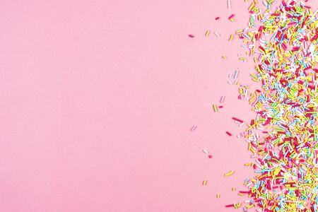 culinary pastry rainbow sprinkles are scattered on a pink background. small sugar sprinkles for decorating cakesの写真素材