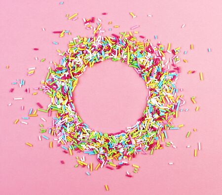 culinary pastry rainbow sprinkles are scattered on a pink background. small sugar sprinkles for decorating cakes are laid out in a circleの写真素材