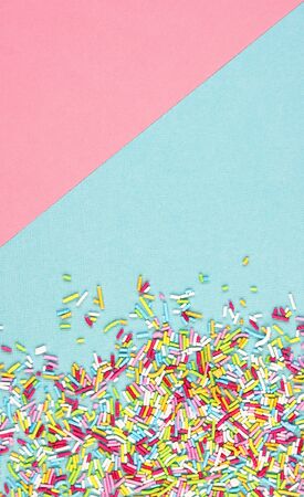 culinary pastry rainbow sprinkles are scattered on a pink and blue background. small sugar sprinkles for decorating cakesの写真素材