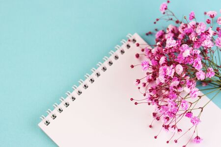 purple flowers with a Notepad on a blue background top view. a white notebook with a spring flower bouquet.の写真素材