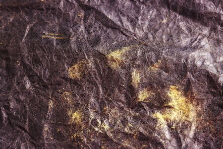 black crumpled surface with gold streaks for the background. black crumpled paper with yellow stripes top viewの写真素材