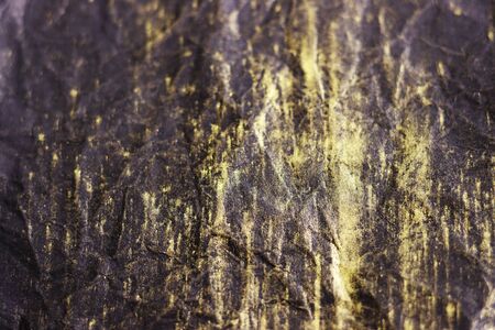 black crumpled surface with gold streaks for the background. black crumpled paper with yellow stripes top viewの写真素材