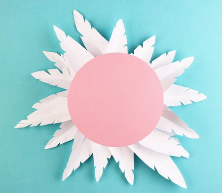 white paper feathers on a blue background, top view. paper decoration with a pink circle on a pastel backgroundの写真素材