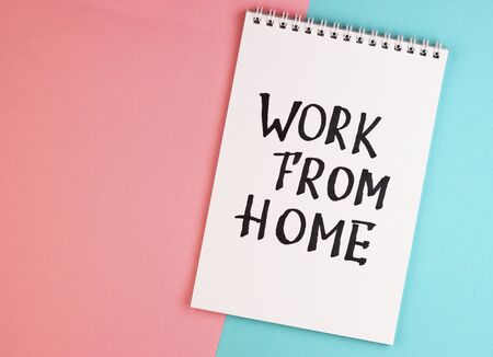 white notebook with the text work at home, top view. pink and blue background with Notepadの写真素材