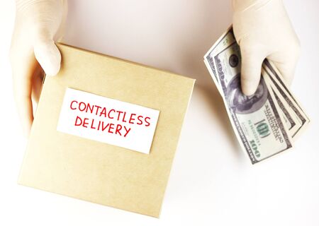 gloved hands pass a gift box with the text of contactless delivery and money. image of a secure courier delivery on a white backgroundの写真素材