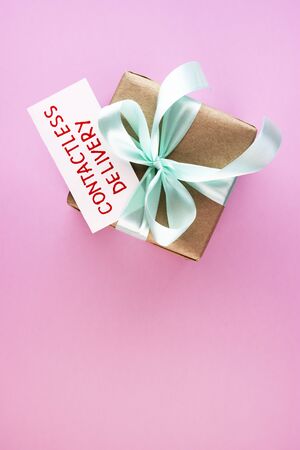 gift box with text contactless delivery on a pink background. secure courier delivery. paper parcel with blue ribbonの写真素材