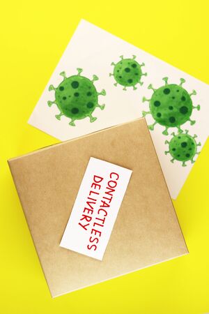 box with the text of the contactless delivery of the top view. brown postal parcel with a picture of coronavirus on a yellow backgroundの写真素材