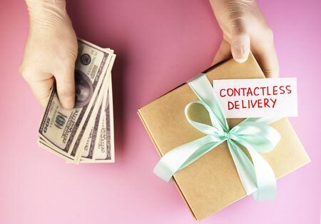 gloved hands pass a gift box with the text contactless delivery. image of a secure courier delivery on a pink backgroundの写真素材