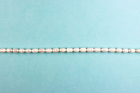 women's accessories made of pearls on a blue background, top view. white pendant made of precious stones. pastel background for women's daysの写真素材