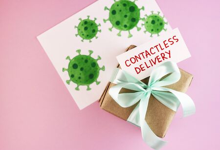 gift box with text contactless delivery on a pink background. secure courier delivery. paper parcel with blue ribbonの写真素材