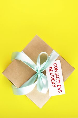 gift box with text contactless delivery on a yellow background. secure courier delivery. paper parcel with blue ribbonの写真素材