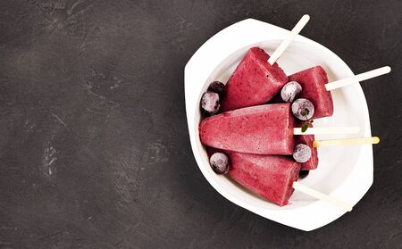 frozen red ice cream on a stick with chunks of ice and cherries in a white plate on a black background. cherry strawberry watermelon ice cream with dry ice on the tableの写真素材