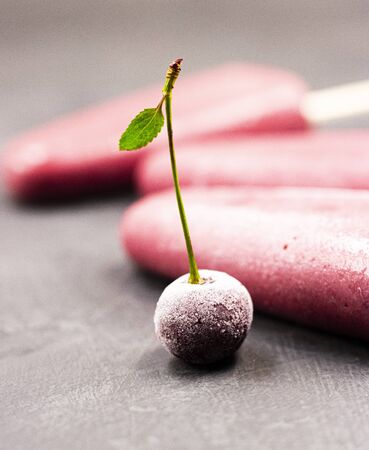 frozen red ice cream on a stick with a cherry in close-up on a black background. cherry strawberry watermelon sundaeの写真素材