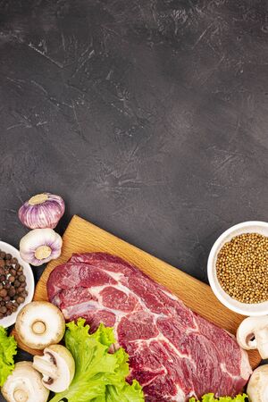 Raw fresh marble meat steak and seasonings on a dark marble background, top view. fresh greens with mushrooms, garlic and beefの写真素材