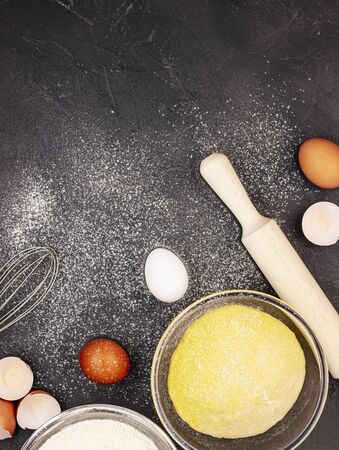 Dark marble background strewn with white baking flour with whole and beaten eggs, dough and rolling pin, top view. The concept of cooking dumplingsの写真素材