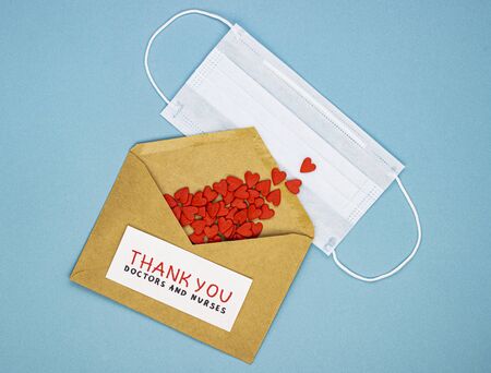 medical mask with red hearts spilled out of the envelope and the inscription thank you doctors and nurses. the concept of gratitude to hospital employees, heroes in the fight against diseasesの写真素材