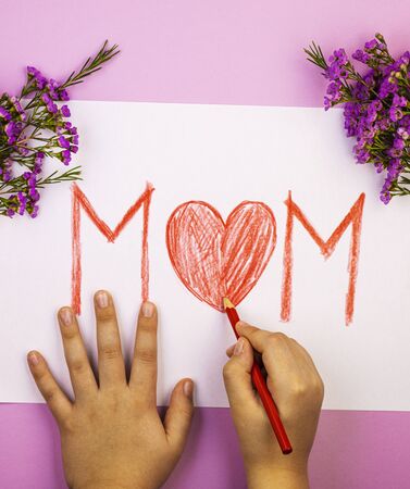hands make a red pencil card for mom with mother's day, top view. the inscription mother with a big red heart. bouquet of wild flowers with a postcardの写真素材