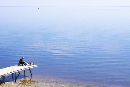 a lone fisherman on the Bank of a large river of the sea. the concept of a summer hobby hobby fishing with a fishing rodの写真素材