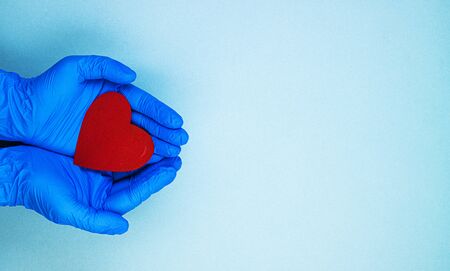 red heart in hands in blue medical gloves on a blue background. background for the day of the medic, top view, space for textの写真素材