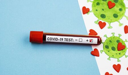 an ampoule with a positive test for covid-19 and a picture of a coronavirus with small hearts on a blue background, top view. concept of blood donation for the coronavirus testの写真素材