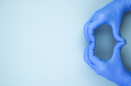 heart sign with hands in blue medical gloves, top view. men's hands represent love on a blue...
