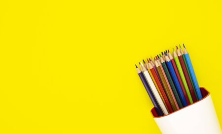 colored pencils in a white organizer, isolated on a yellow background. office supplies for preparing for school. background for designers with space for textの写真素材