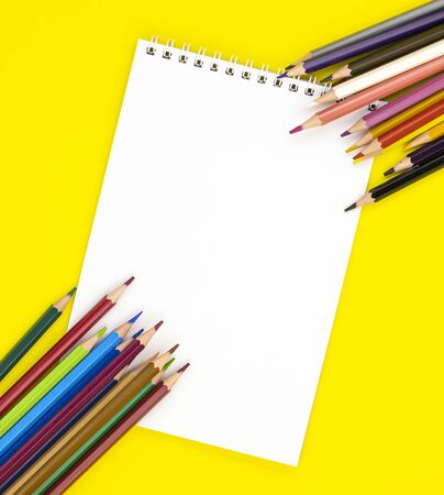 white blank Notepad in the center and colored pencils in the corners, isolated on a yellow background. stationery for school preparation. background for designers with space for text. online learningの写真素材