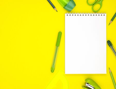 white blank Notepad with green school stationery isolated on a yellow background, top view. background for designers with space for text. online learningの写真素材